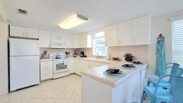 52 Palm Dr, Ormond Beach, FL 32176 - kitchen featuring white appliances, decorative backsplash, a peninsula, white cabinetry, and light tile patterned flooring