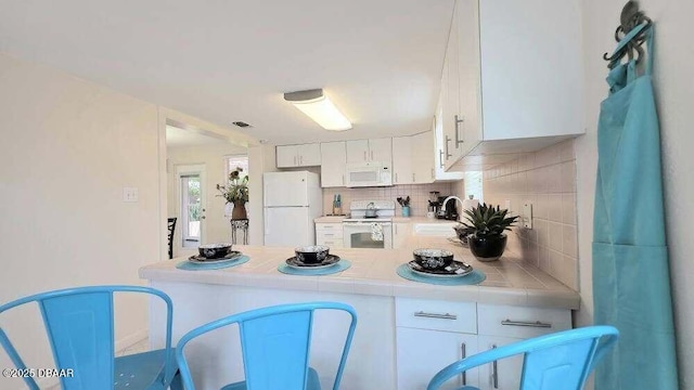 52 Palm Dr, Ormond Beach, FL 32176 - kitchen featuring white appliances, tile countertops, tasteful backsplash, white cabinets, and a peninsula