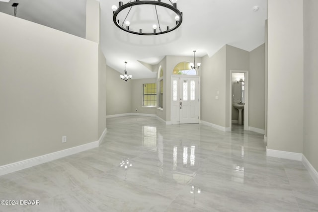 entrance foyer featuring high vaulted ceiling, marble finish floor, baseboards, and an inviting chandelier