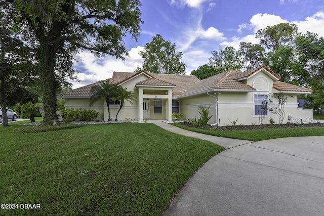 mediterranean / spanish-style house with stucco siding, a tile roof, and a front yard