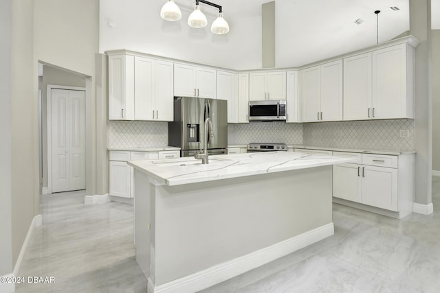 kitchen featuring stainless steel appliances, tasteful backsplash, a sink, an island with sink, and light stone countertops