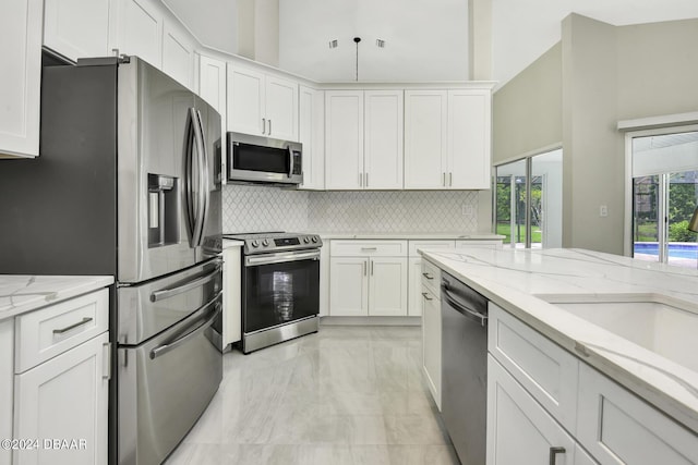 kitchen featuring appliances with stainless steel finishes, white cabinets, backsplash, and a towering ceiling