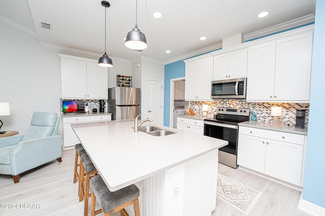 kitchen with a kitchen bar, stainless steel appliances, decorative light fixtures, white cabinets, and an island with sink