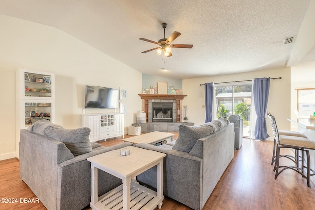 living room featuring lofted ceiling, hardwood / wood-style flooring, ceiling fan, a textured ceiling, and a tiled fireplace