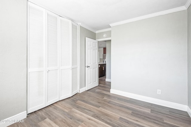 unfurnished bedroom with wood-type flooring, ornamental molding, and a closet