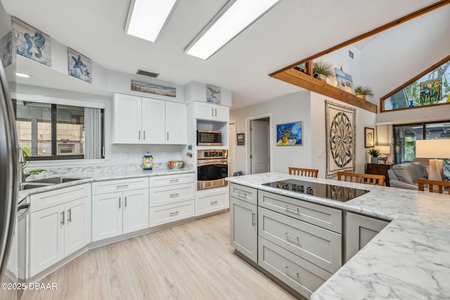 kitchen featuring appliances with stainless steel finishes, white cabinetry, sink, light wood-type flooring, and light stone counters