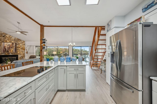 kitchen with stainless steel refrigerator with ice dispenser, light hardwood / wood-style flooring, a stone fireplace, ceiling fan with notable chandelier, and black electric cooktop