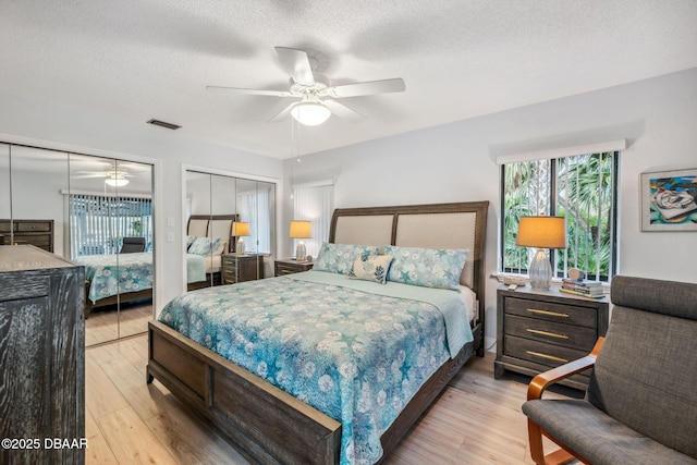 bedroom featuring ceiling fan, multiple closets, a textured ceiling, and light hardwood / wood-style floors