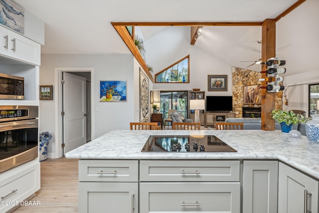 kitchen with a fireplace, lofted ceiling with beams, white cabinetry, appliances with stainless steel finishes, and light stone counters