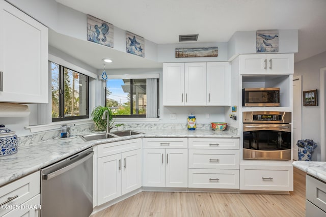 kitchen featuring stainless steel appliances, white cabinetry, light stone counters, and sink