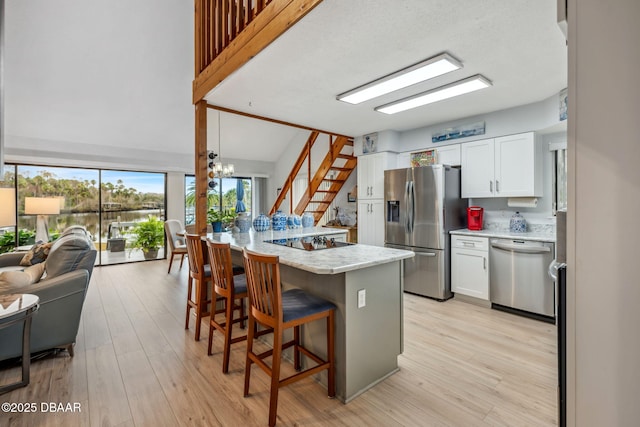 kitchen featuring a breakfast bar, white cabinetry, hanging light fixtures, light stone countertops, and appliances with stainless steel finishes