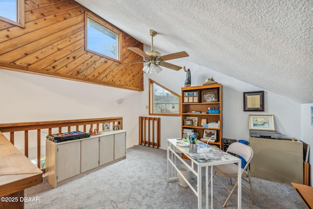 carpeted home office with ceiling fan, vaulted ceiling with skylight, and a textured ceiling