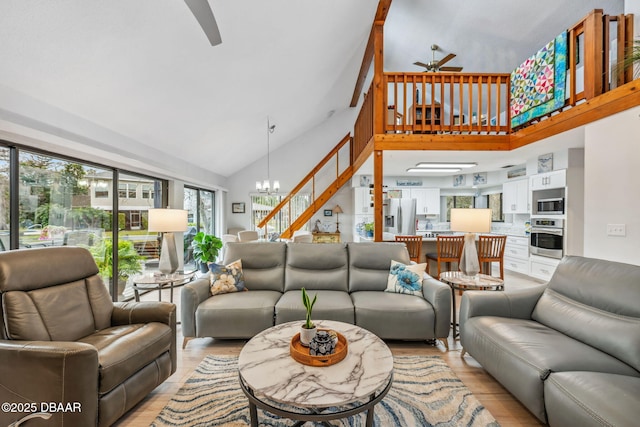 living room featuring light wood-type flooring, ceiling fan with notable chandelier, and high vaulted ceiling