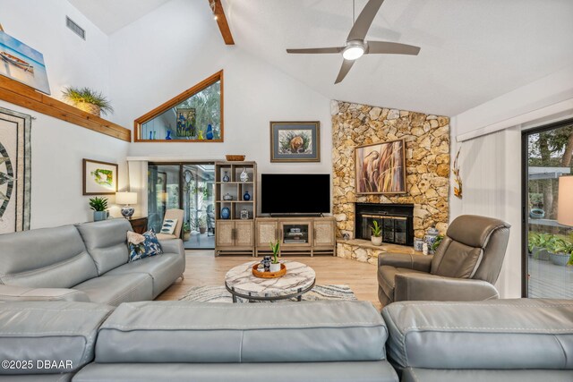 living room featuring beamed ceiling, a stone fireplace, hardwood / wood-style flooring, high vaulted ceiling, and ceiling fan