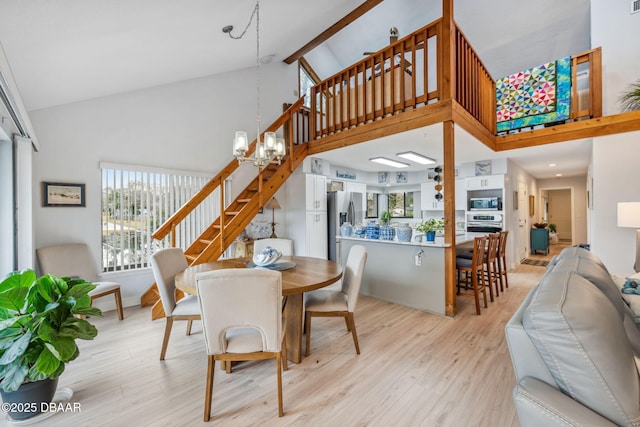 dining space with an inviting chandelier, a fireplace, light hardwood / wood-style flooring, and high vaulted ceiling