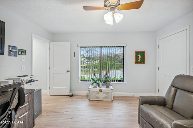 living area with ceiling fan, light wood-type flooring, and a textured ceiling