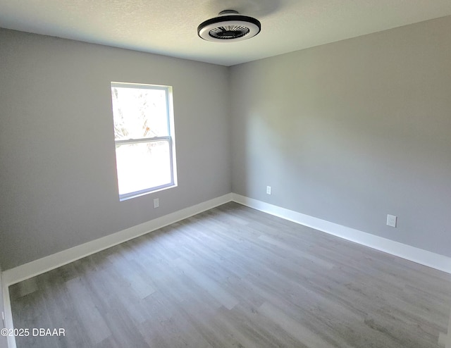 empty room featuring a textured ceiling, baseboards, and wood finished floors