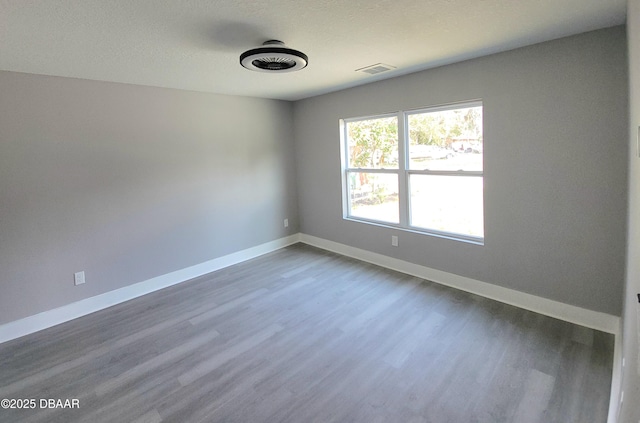 unfurnished room with visible vents, a textured ceiling, baseboards, and wood finished floors