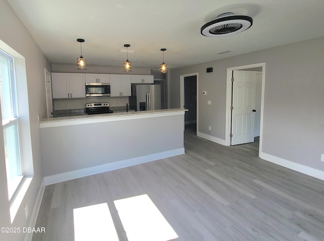 kitchen with appliances with stainless steel finishes, light wood-type flooring, white cabinets, and a peninsula