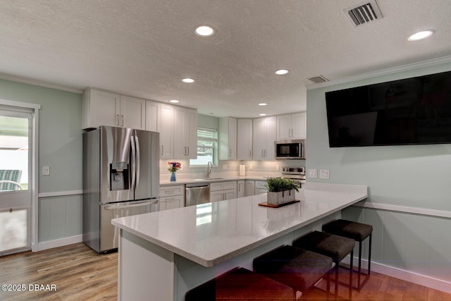2917 Carriage Dr, South Daytona, FL 32119 - kitchen featuring stainless steel appliances, a textured ceiling, light wood-style flooring, a kitchen bar, and a peninsula