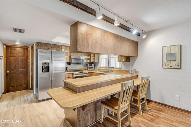 kitchen featuring sink, stainless steel appliances, light hardwood / wood-style flooring, kitchen peninsula, and track lighting