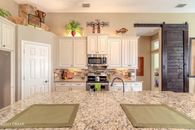 kitchen with stainless steel appliances, light stone counters, a barn door, tasteful backsplash, and sink