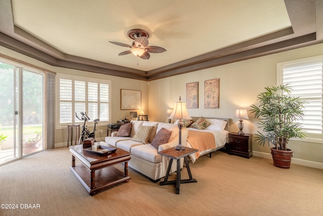 carpeted bedroom featuring multiple windows, a raised ceiling, ceiling fan, and access to exterior