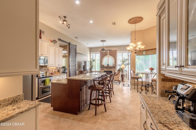 kitchen featuring stainless steel appliances, cream cabinets, light stone countertops, a breakfast bar area, and decorative light fixtures