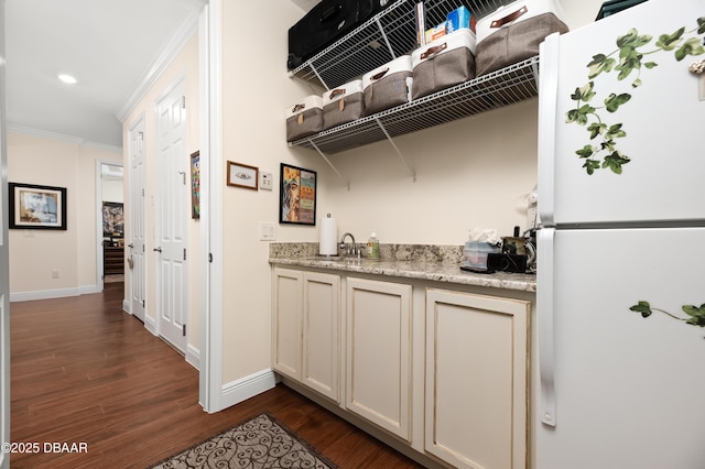 kitchen featuring dark wood-type flooring, ornamental molding, white refrigerator, light stone counters, and sink