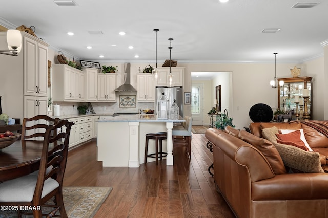 kitchen featuring decorative light fixtures, tasteful backsplash, a kitchen island, stainless steel fridge, and wall chimney exhaust hood