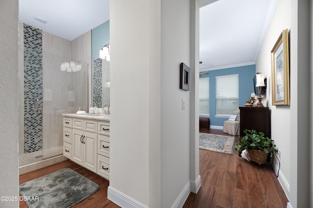 bathroom featuring crown molding, tiled shower, wood-type flooring, and vanity