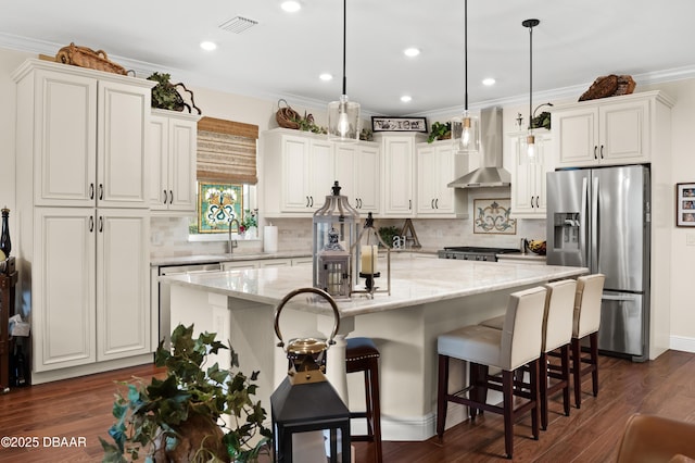 kitchen featuring pendant lighting, stainless steel fridge, wall chimney exhaust hood, and a kitchen island with sink