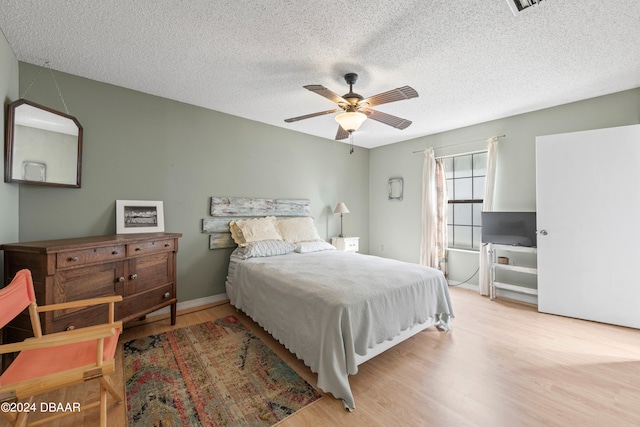 bedroom with a textured ceiling, light hardwood / wood-style floors, and ceiling fan