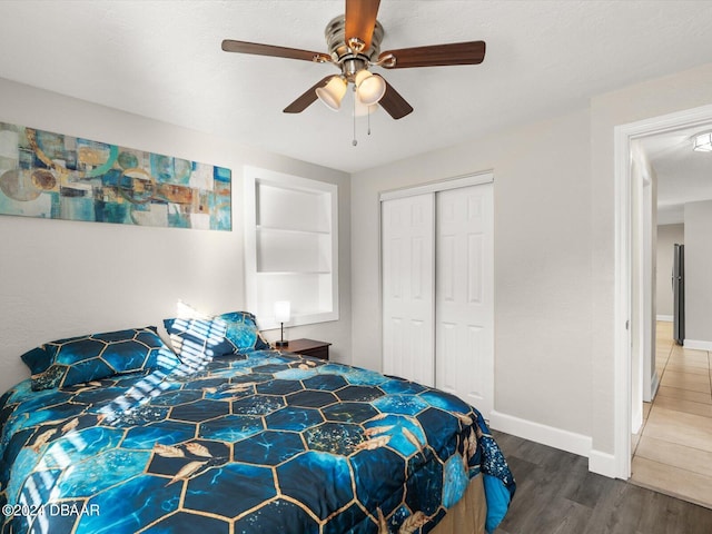 bedroom with baseboards, ceiling fan, freestanding refrigerator, wood finished floors, and a closet