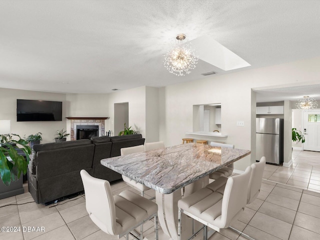 dining room with visible vents, an inviting chandelier, a skylight, light tile patterned floors, and a tile fireplace