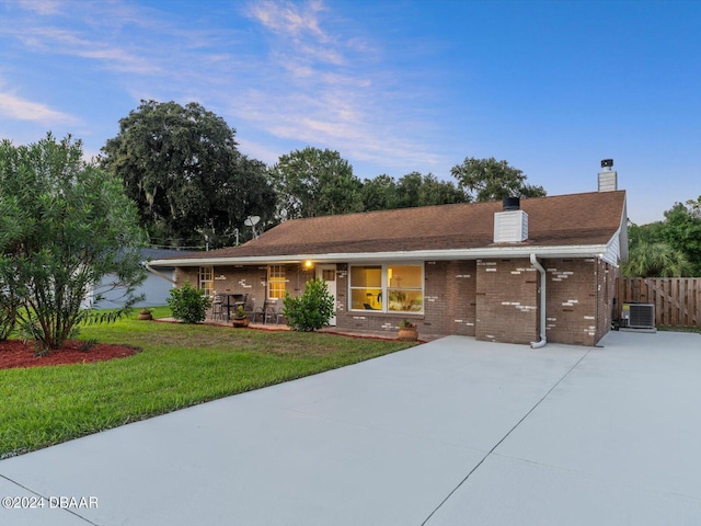 single story home featuring a front lawn, central AC, fence, brick siding, and a chimney