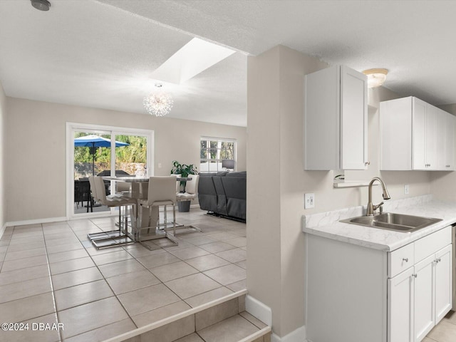 kitchen with baseboards, a skylight, light tile patterned flooring, a sink, and white cabinets