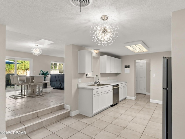 kitchen with a chandelier, light countertops, freestanding refrigerator, white cabinetry, and a sink