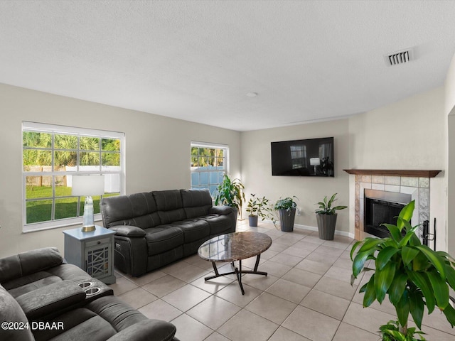 living area with a tiled fireplace, light tile patterned flooring, visible vents, and a textured ceiling