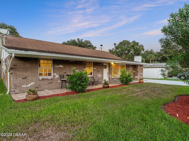 ranch-style house featuring a patio, a front lawn, brick siding, and a chimney