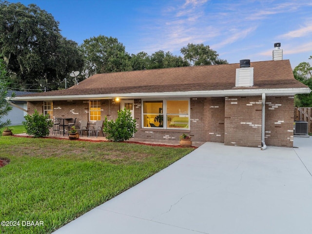 ranch-style house with a front lawn, brick siding, central AC unit, and a chimney