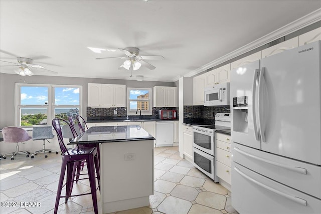 kitchen with sink, a kitchen breakfast bar, white cabinets, white appliances, and a center island