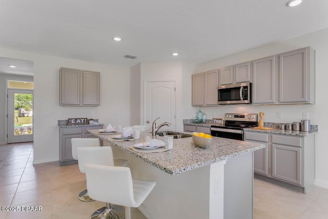 kitchen with gray cabinets, light tile patterned flooring, appliances with stainless steel finishes, sink, and a center island with sink