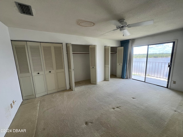 unfurnished bedroom featuring access to outside, light colored carpet, a textured ceiling, ceiling fan, and multiple closets