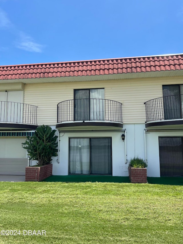 back of house featuring a lawn and a balcony