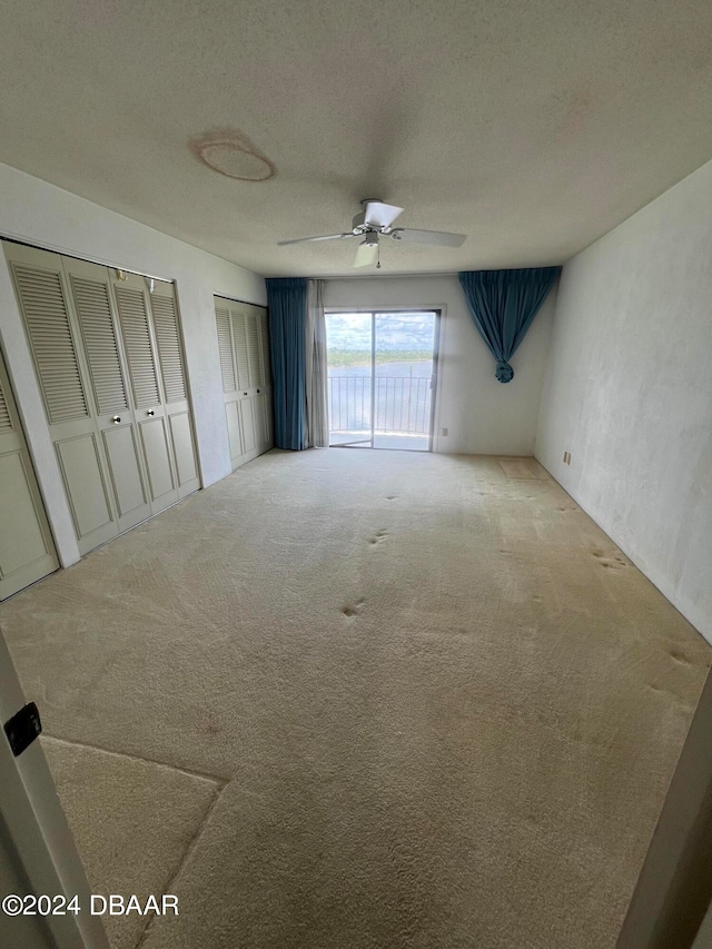 unfurnished bedroom with light carpet, ceiling fan, a textured ceiling, two closets, and access to outside