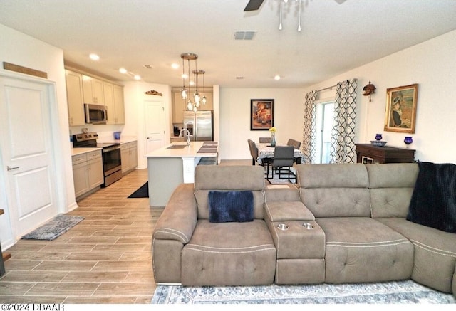 living room with ceiling fan, sink, and light wood-type flooring