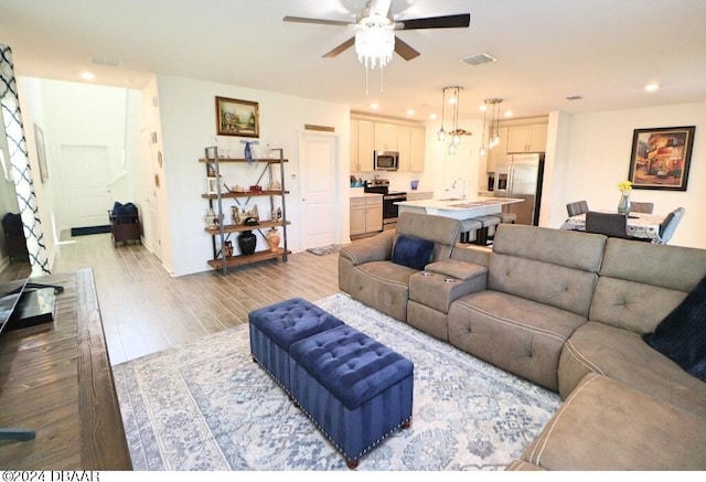 living room with light hardwood / wood-style floors, ceiling fan, and sink