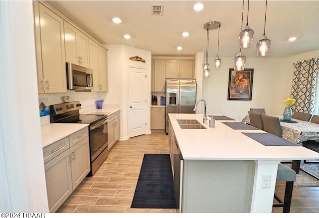 kitchen featuring a center island with sink, appliances with stainless steel finishes, hanging light fixtures, sink, and a breakfast bar area