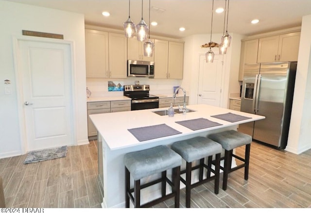 kitchen with pendant lighting, appliances with stainless steel finishes, sink, and an island with sink